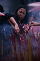 Young woman lighting incense at temple.