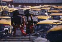 Porters carrying luggage on their heads through parked taxi cabs at New Delhi railway station.