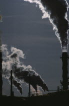 Smoke from industrial chimneys silhouetted against sun.