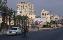 Children on quiet road with billboard of Yasser Arafat and city buildings behind.