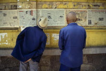 Two men reading newspapers displayed on wall.