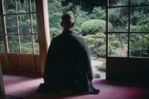 Zen Buddhist monk meditating in front of screen open to garden.