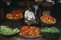 Vendor at roadside stall selling okra  tomatoes and aubergines.