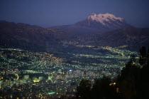 Illuminated cityscape and snow capped peak of Mount Illimani at dusk.