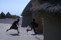 Shilluk children running towards thatched village hut.
