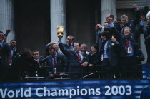 The winning Rugby World Cup 2003 team on top of a bus holding the trophy during a celebratory procession