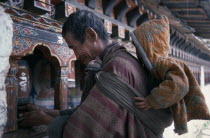 Man with child on his back placing butter on a prayer wheel as an offering