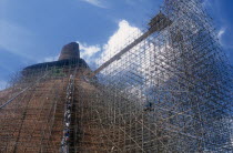 Jetavanarama dagoba.  Huge brick dome undergoing reconstruction.  Line of workers on network of scaffolding covering exterior.