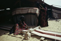 Bedouin women weaving and spinning outside tent.