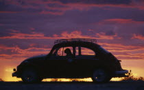 VW Beetle in silhouette against dramatic sunset sky.