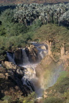 Water gushing through layers of rocky cliffs into fast flowing river below.