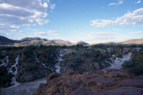 Water gushing through rocky cliffs into fast flowing river.