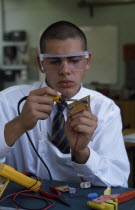 Schoolboy in electronics class wearing protective glasses during practical experiment.