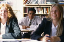 Male and female pupils smiling working at desks in a classroom.