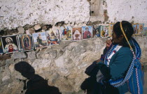Woman in front of coloured pictures of the lives of the Saints and Christ displayed along stone wall.