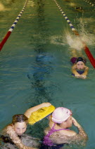 Three girls at swimming club practice in pool with floats.