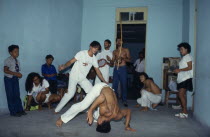 Local men in animated poses of martial arts  inside a small room with spectators.