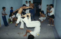 Local men in animated poses of martial arts  inside a small room with spectators.