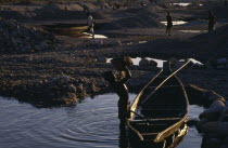 Workers in stone quarry near water with man in foreground lifting basket of stones from wooden rowing boat.