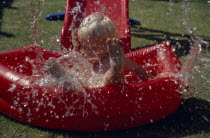 Young boy splashing in a red inflatable paddling pool.