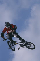 Cyclist twisting bike in mid air against blue sky and clouds.