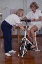 Female sport physiotherapist with female patient on exercise bike