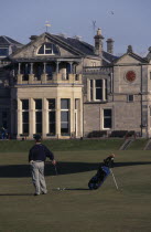 Golfer standing on green outside St. Andrews golf course clubhouse