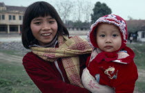 Portrait of girl holding baby dressed  in red jacket and bonnet
