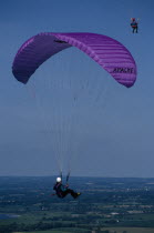 Paraglider with purple chute and landscape below.