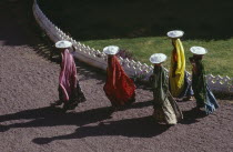 Aerial view over female construction workers carrying building materials on their heads.