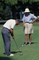 New Zealand. North Isalnd. Taupo. Middle aged couple on a putting green with man taking a putt. .