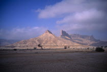 Desert landscape with triangular rock formation and pinnacles in sunlight