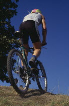Mountain biker on crest of hill seen from behind.