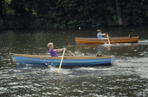 Two boys in wooden boats competing in rowing race on the River Thames