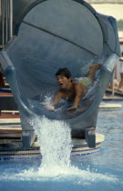 Boy sliding head first down water slide in pool