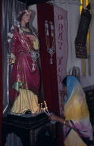 Indian woman lighting candles in front of statue of religious figure at Christmas.