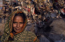 Female rubbish recycler.  Head and shoulders portrait with rubbish tip behind.