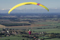 Paraglider with yellow chute and landscape below.