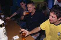 Three young men smoking and drinking in bar.