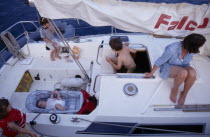 Greece. View over a family on a sailing holiday aboard their yacht. Mother with children and a baby lying in a carry cot