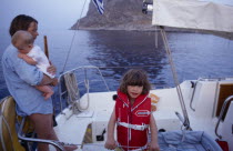 Greece. Monemvasia. An English family on a sailing holiday aboard their yacht. Mother holding a baby near a young girl wearing a life jacket