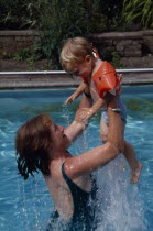 Mother lifting child wearing water wings out of water in swimming pool