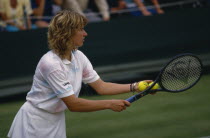 Steffi Graf playing at Wimbledon 1987. Threequarter view in profile to the left  about to serve.