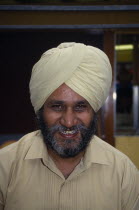 Head and shoulders portrait of a Sikh man smiling wearing a beige turban
