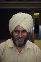 Head and shoulders portrait of a Sikh man smiling wearing a beige turban