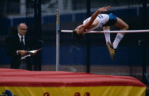 Competitor in junior athletics championships clearing bar in high jump.