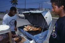 Man cooking jerk chicken on roadside stall with waiting customer.Jamaican Male Men Guy Poulet Volaille West Indies