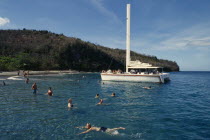 Catamaran tour.  Tourists swimming from moored boat with beach and tree covered headland behind.Beaches Caribbean Holidaymakers Resort Sand Sandy Seaside Shore Tourism West Indies Windward Islands