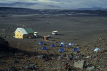 Several blue tents camping in a lava field beside a small buildingIcelandic Nordic Northern Europe