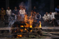 Hindu cremation in Pashupatinath Temple.  Burning wood funeral pyre with onlookers on steps behind.Asia Asian Nepalese Religion Religion Religious Hinduism Hindus